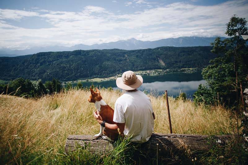 the owner sits with the basenji on the hill